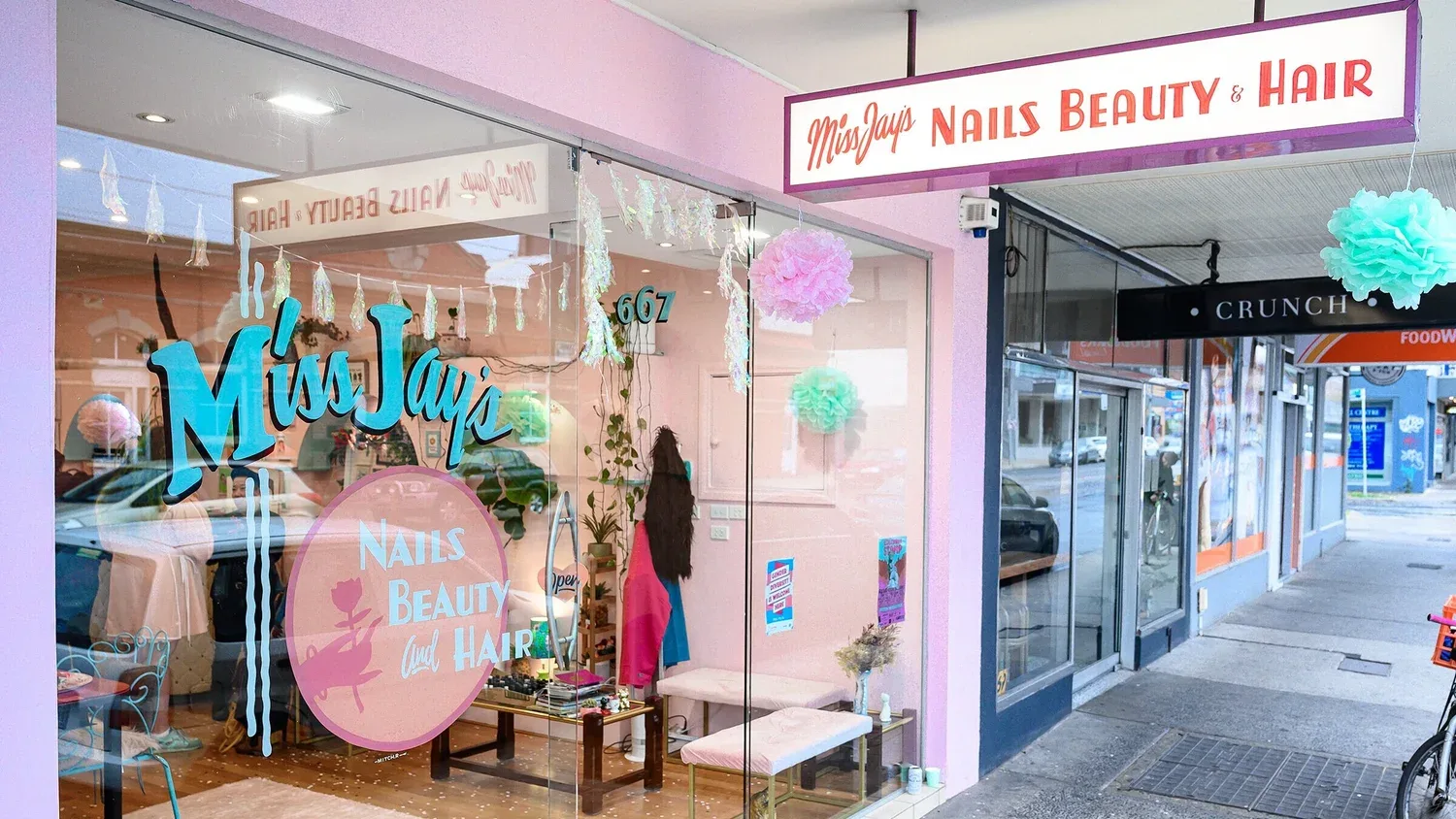 667 High Street Thornbury shopfront — pink render with teal Miss Jay's brush-script window decal, iridescent tinsel garland and pink tissue pom-poms in the glass